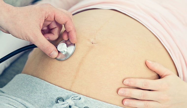 Schwangerer Bauch wird mit Stethoskop untersucht.