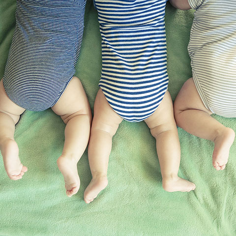 Drei Babys liegen nebeneinander auf dem Bauch. 