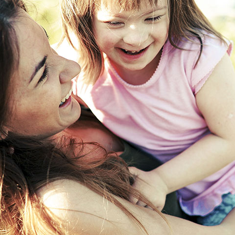 Mutter mit einem Mädchen mit Down-Syndrom auf dem Arm, beide lachend.