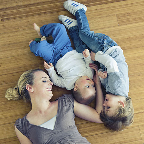 Frau liegt mit zwei Kindern auf dem Boden. 